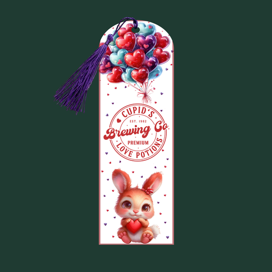"Aluminum bookmark with heart balloons, vintage ‘Cupid’s Brewing Co.’ love potion logo, and a cartoon bunny holding a heart. Purple tassel included."