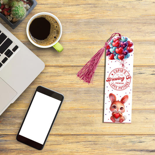 "Aluminum bookmark with heart balloons, vintage ‘Cupid’s Brewing Co.’ love potion logo, and a cartoon bunny holding a heart. Purple tassel included."
