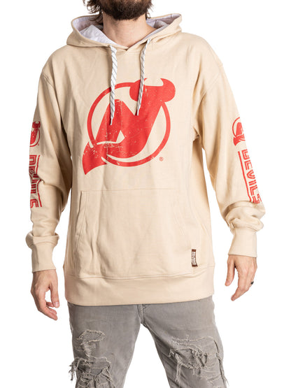 Beige hoodie with red logo and text on sleeves, worn by a person.
