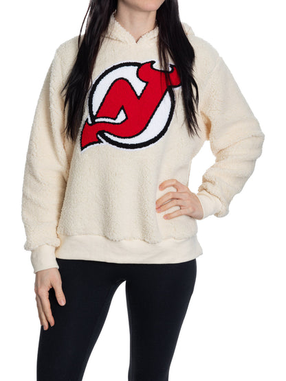 Cream-colored hoodie with a red and black logo worn by a person on a white background